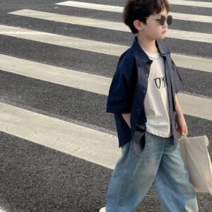 Trendy kid's street-style: A navy open-front shirt layered over a white graphic tee, paired with wide-leg denim jeans and dark sunglasses.